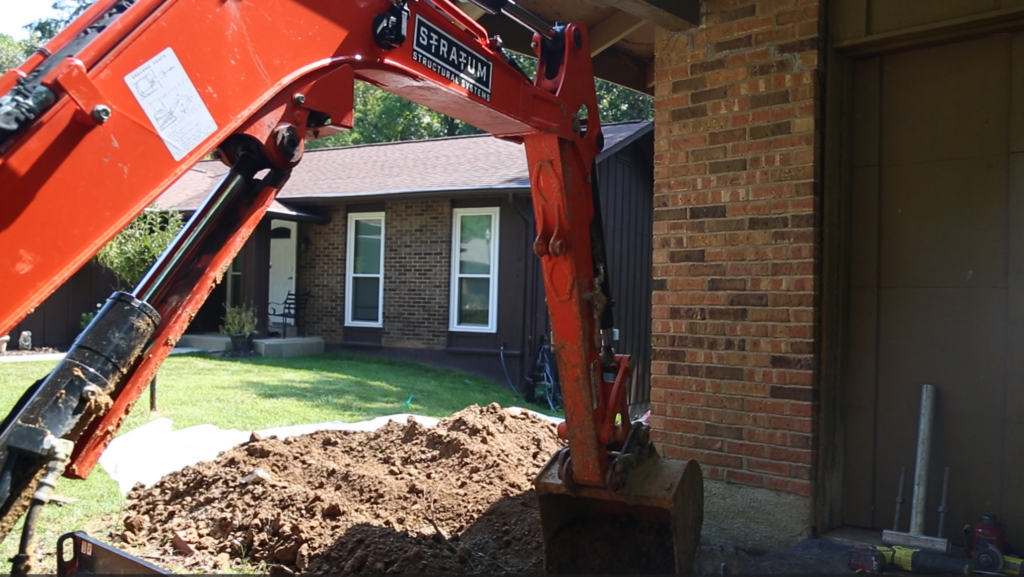 piering excavator working near a home's foundation for repairs